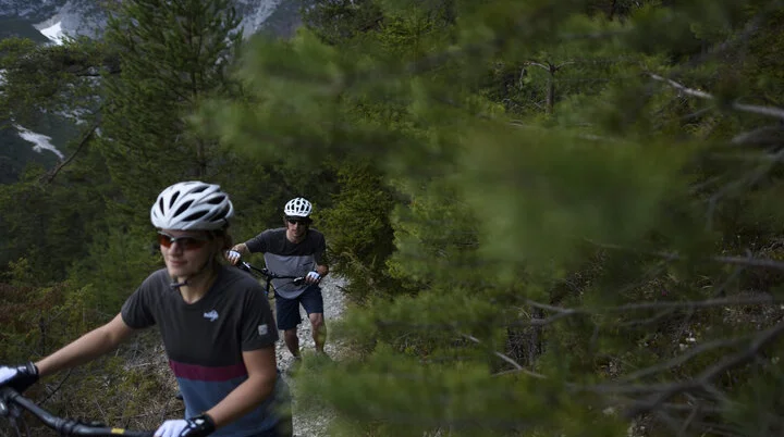 Ein Mountainbiker schiebt sein Rad auf einem Trail in den Bergen. | © DAV/Wolfgang Ehn